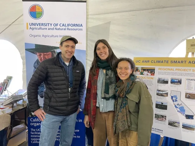 OAI representatives stand in front of posters about the Organic Agriculture Institute and climate-smart agriculture