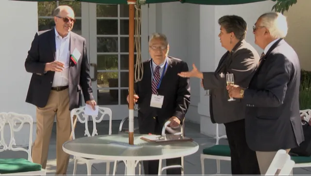 Four people stand with raised glasses of champagne, three looking at Rosenberg as Humiston speaks.