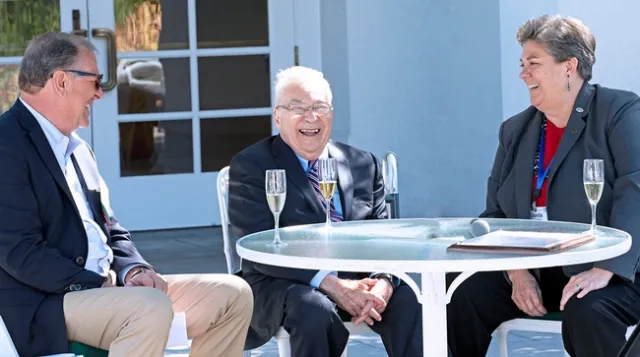 The three people are sitting at a table outdoors.