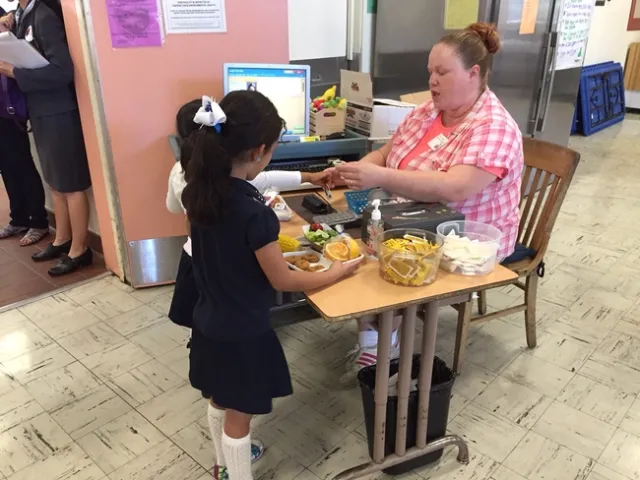 Two girls pay a woman for school lunch.