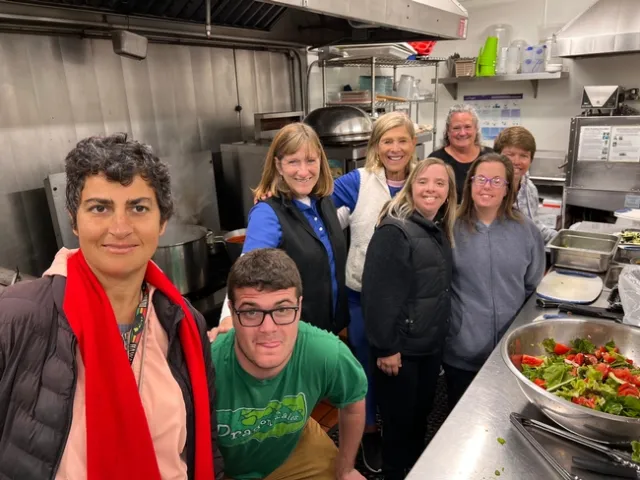 A group of people smiling at the camera while standing in a kitchen, preparing food.