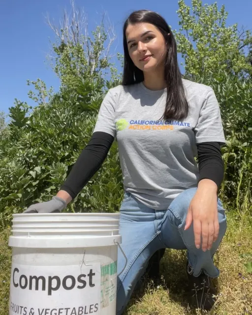 Woman crouching in a field next to a compost bucket