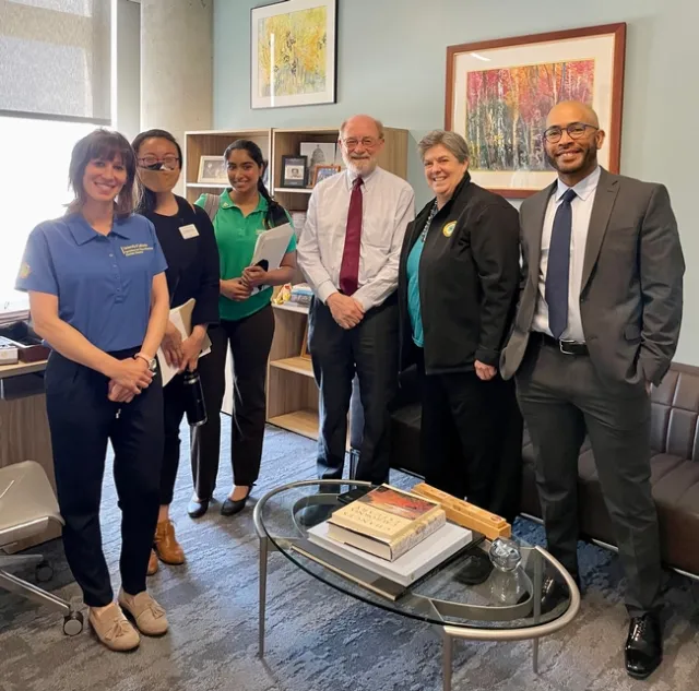 Six people stand in an office with bookshelves behind them.