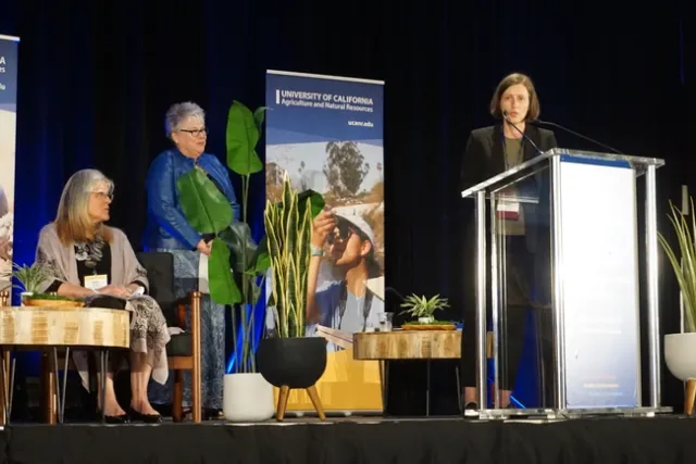 Helen Dahlke, on right, speaks from lectern as Lynn Schmitt-McQuitty and Kathy Eftekhari listen