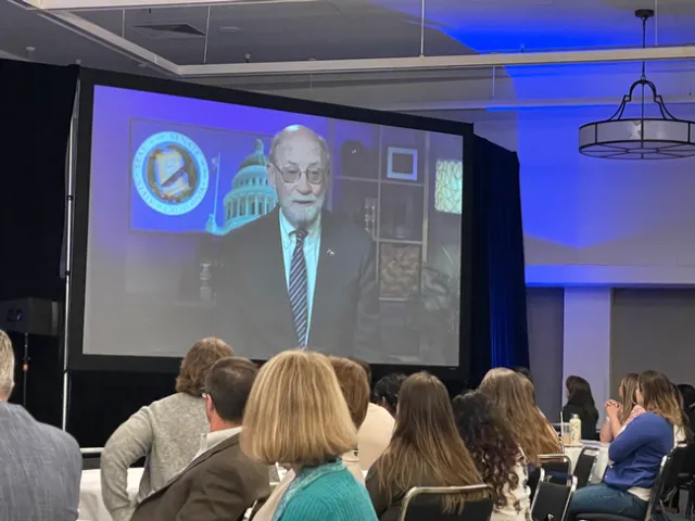People in a conference room view Laird speaking on screem.