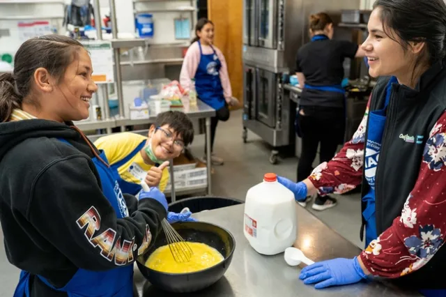 One youth and adult across from each other at a counter, cooking eggs
