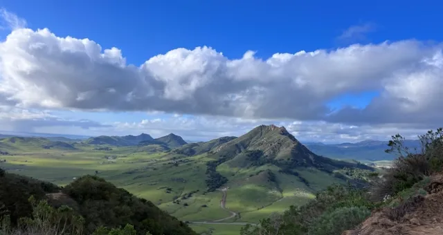 Landscape with green grass, sharp peaks and blue skies with clouds.