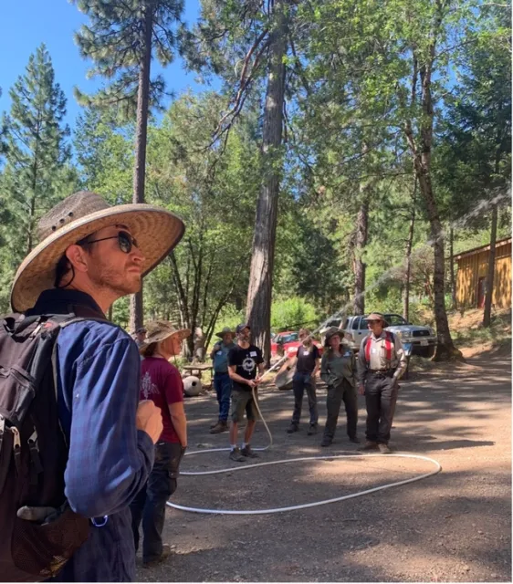 View of a man holding a hose, shooting water upwards, while surrounded by others who are observing him.