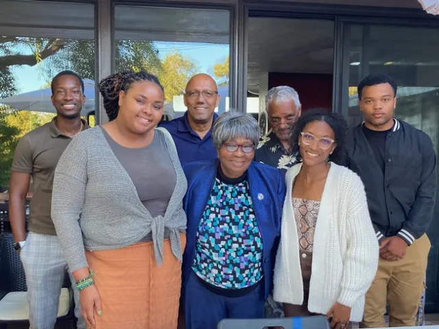 The group stands in front of sliding glass doors that reflect leafy trees