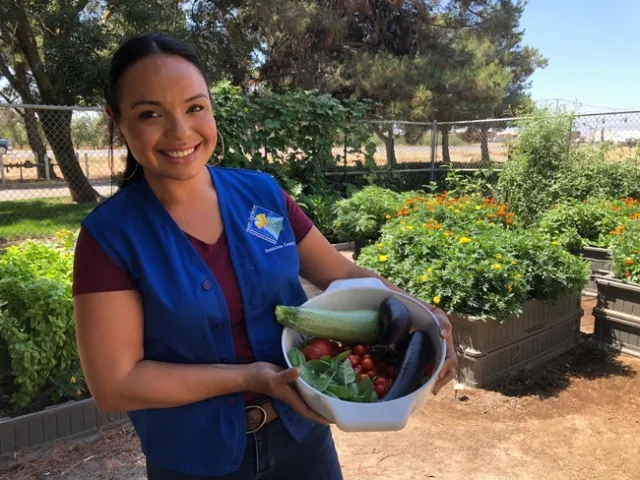 Smiling woman wearing a blue vest standing in a garden.