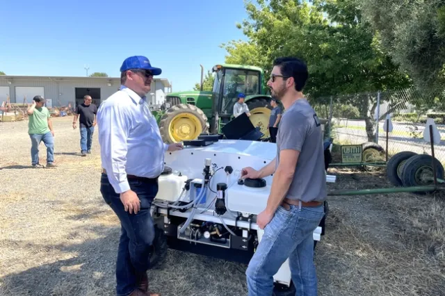 Gabe Youtsey converses while standing next to a robot with agricultural applications