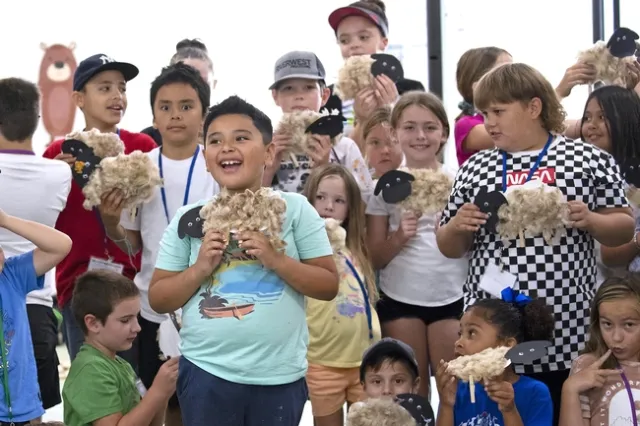 Kids hold up their paper sheep, crafted from freshly sheared wool
