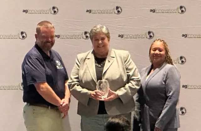 Glenda holds a crystal trophy while flanked by a man and woman.