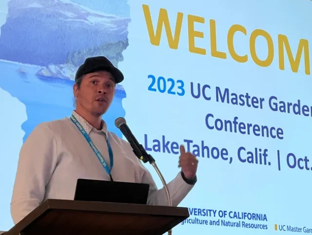 Man giving a speech at podium in front of welcome to the conference signage.