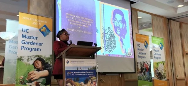 Woman speaking in front of podium with a screen showing a presentation behind her.