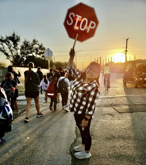 A woman holds a stop sign in a crosswalk as people walk and bike by