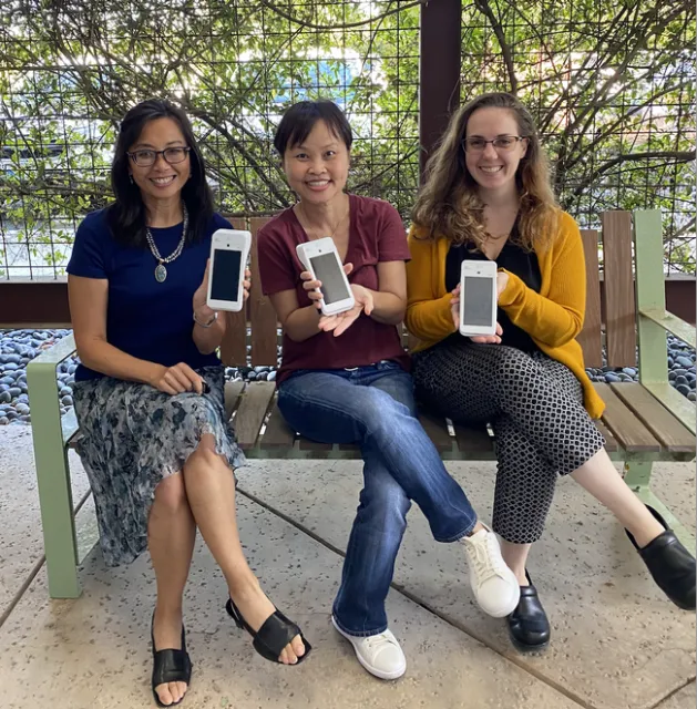 Three women sit holding credit card scanners that look like cell phones.