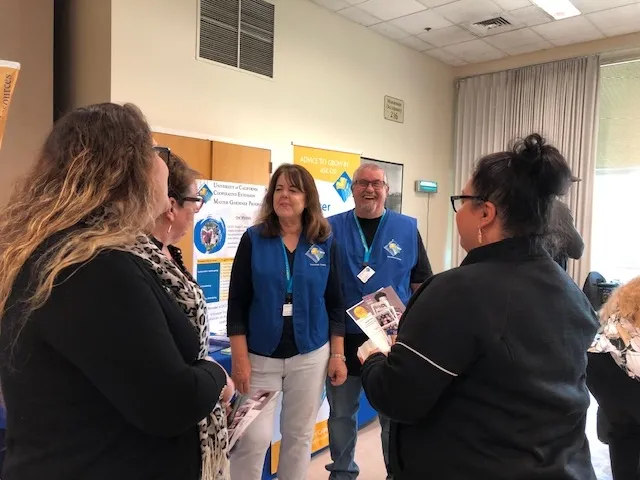 Two people at a booth smiling while speaking to attendees.