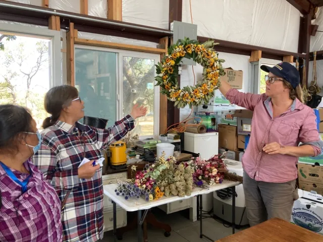 Lauren holds up a wreath made of greens and yellow flowers.