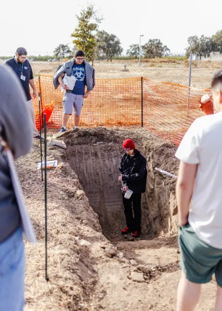A student digs into the side of the soil pit.
