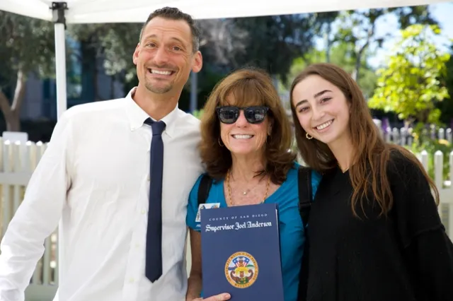 Three people stand shoulder to shoulder and smile at the camera.