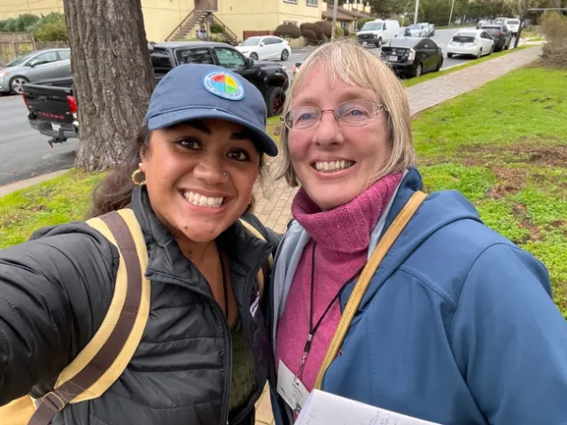Saoi Sope, wearing an Organic Ag Institute hat, and Annemiek Schilder grin for a selfie near a street.