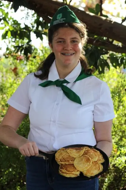 A middle-school girl holds a pan with homemade pancakes on it.