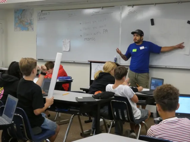 An educator points to a whiteboard in front of a classroom of students