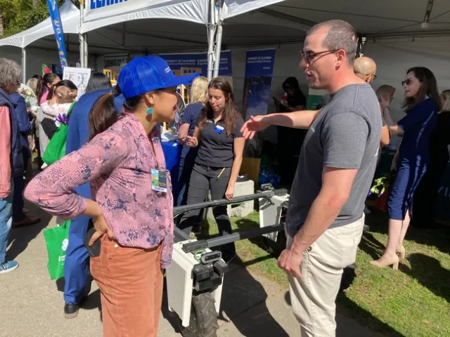 Reyes listens as a man speaks and gestures toward the Amiga robot.