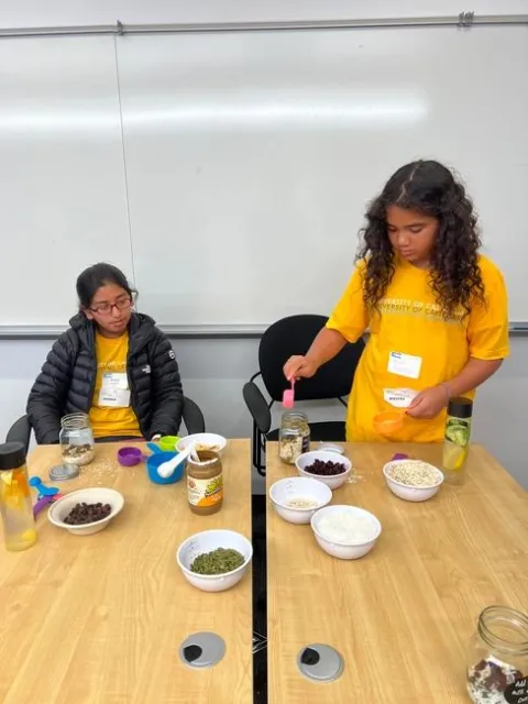 Two girls add ingredients to their oatmeal recipe.