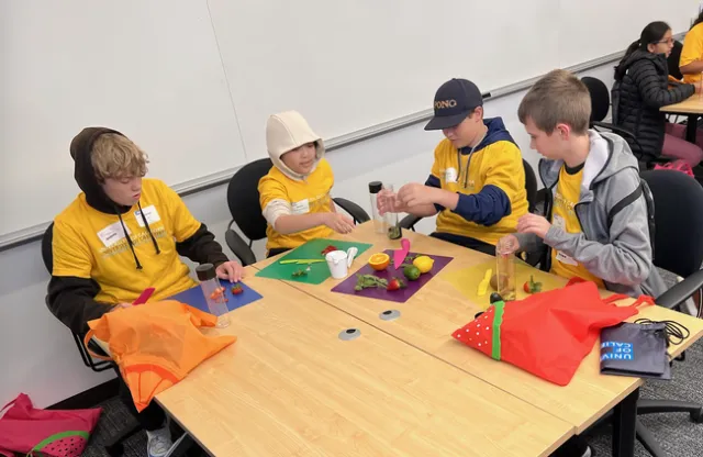 Four kids in yellow UC shirts slice citrus and berries to put in reusable bottles.
