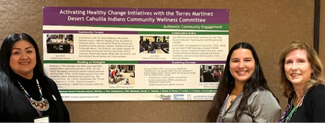 Three women stand in front of a poster that says,