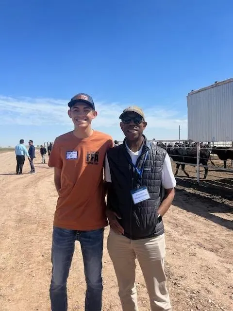 Young man stands next to President Drake with cows in the background.