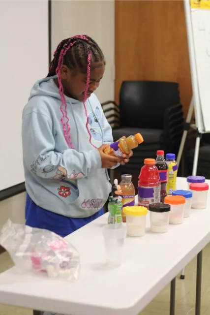 A young girl reads the back of an orange juice bottle.