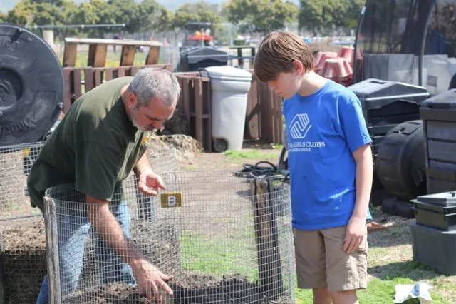 A middle-aged man and young boy look down at a pile of compost.