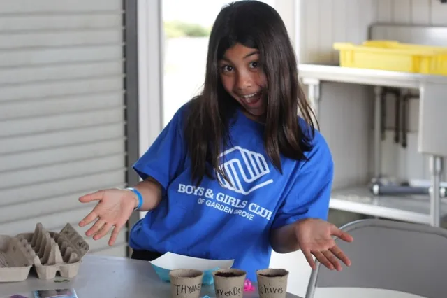 A young girl smiles big while presenting her three plants of thyme, lavender and chive.