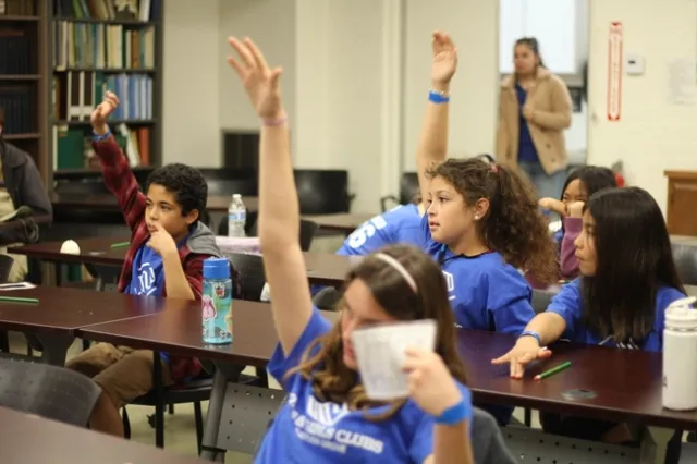 Students raise their hands while sitting down.