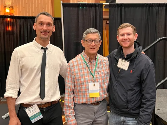 Three men stand side by side and smile at the camera.