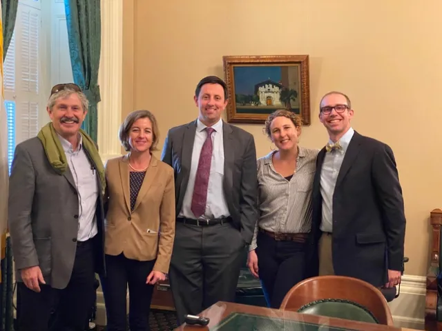 Five people wearing suits pose standing. Ryan's gold bowtie has black and white stripes that coordinate with Lenya's striped blouse.