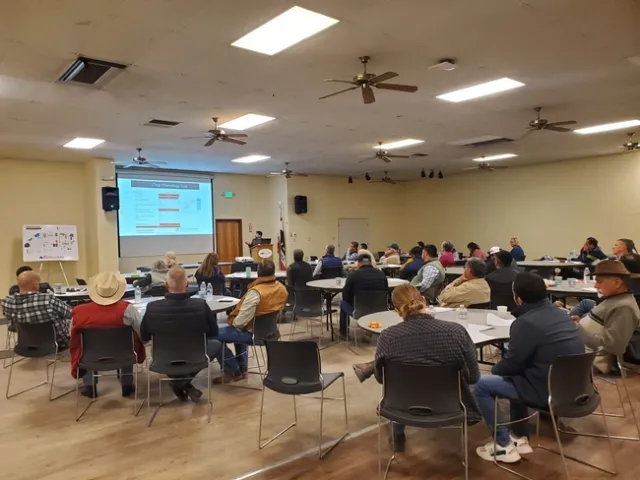 A room full of mostly men sitting around round tables look at a PowerPoint slide as Tapan Pathak describes a crop phenology tool.