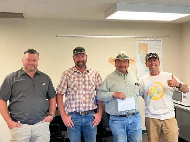 Four men stand in a line. A map of California is on the wall in the background.