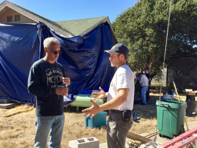 Lewis and Sutherland stand in front of a tarped structure