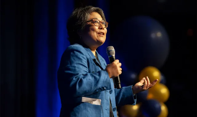 Woman in glasses, Carolyn Dewa, speaking into a mic