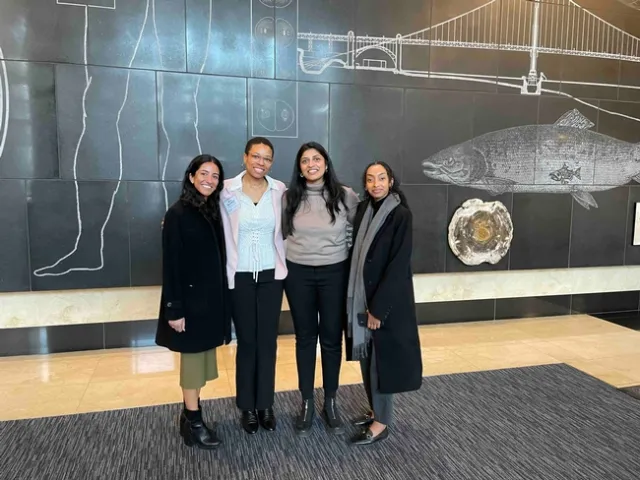 4 women standing together in front of a black background wall mural