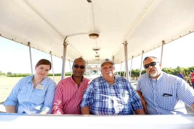 Four people sit in an open air shuttle with vineyards in the background.