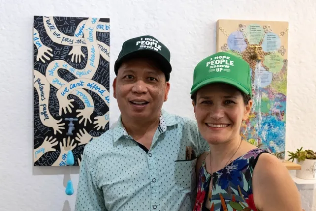 Jolly and Edith pose in front of water-themed art, wearing matching trucker hats that read: