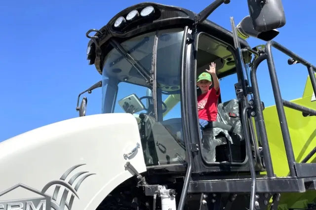 A boy sits in the cab of a harvester