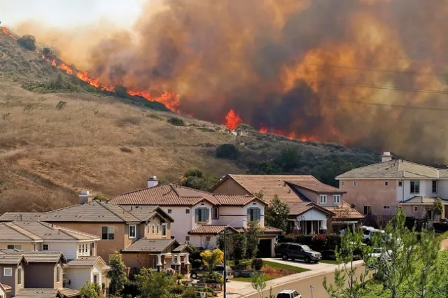 Flames and smoke line a hillside behind a street of houses.