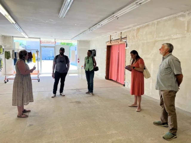 People talk in an empty commercial space as light comes through the front windows