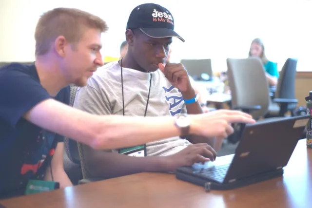 Adult pointing at laptop screen in front of youth